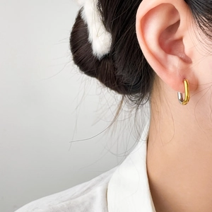 Macro shot of two-tone U-shaped earrings in polished gold and silver steel on ear