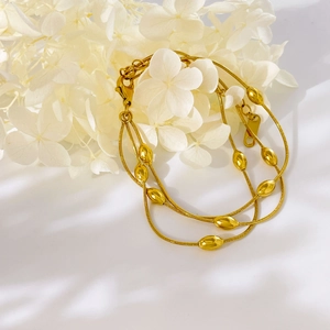 Detail of layered gold snake chain bracelet with polished olive beads on white table