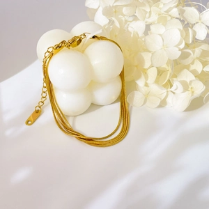 Detailed view of triple-layered gold snake chain bracelet on white decorative candle