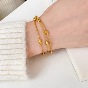 Elegant multi-layer gold snake chain bracelet with oval bean charms on a female wrist