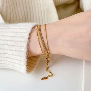 Close-up of triple-layered gold snake chain bracelet featuring K18 engraved tag