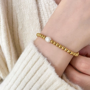 Gold beaded bracelet featuring a central freshwater pearl worn on a wrist over a knit sweater