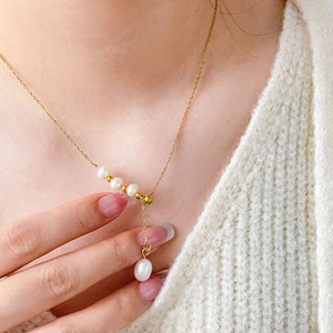 Elegant gold Y-shaped necklace with white freshwater pearls worn on a white sweater