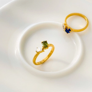 Macro view of 18K gold plated bypass rings with oval green and teardrop white zircon stones
