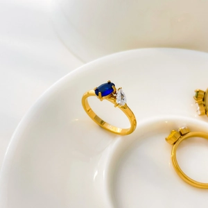 Close-up of dual stone ring with blue oval and clear teardrop zircon on gold band