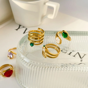 Close-up of golden snake ring with green zircon and red heart gemstone on glass plate