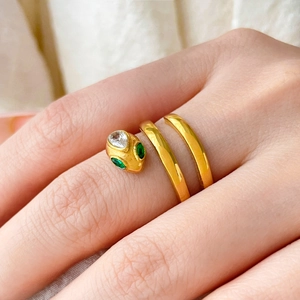 Macro view of gold-plated snake ring with green zircon eyes and clear crystals on finger