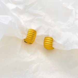 Close-up of gold pumpkin-textured hoop earrings on white wrinkled paper background