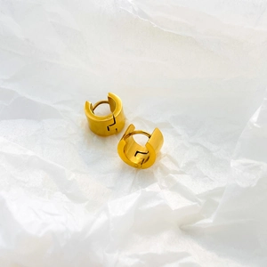 Detailed close-up of chunky gold hoop earrings on textured white paper background