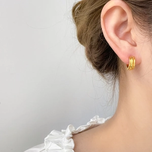 Macro detail of triple-layered golden curved hoop earrings on model ear showing glossy finish