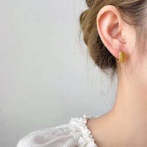 Macro detail of golden curved C-shape earrings with vintage textured pumpkin ridges