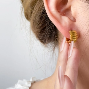 Macro shot of gold ribbed C-shape earrings with vintage textured surface on ear