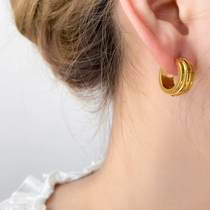 Macro view of gold-plated triple-layered curved hoop earrings with polished pumpkin texture