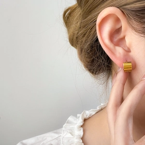 Close-up of a wide polished gold curved hoop earring worn on model for size and style detail