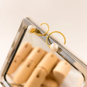 Detalle macro de pendientes de aro dorados con perlas blancas colgados en un espejo