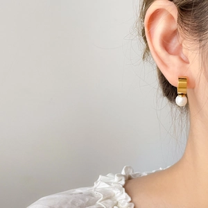 Detalle de pendiente rectangular dorado con una sola perla blanca redonda elegante