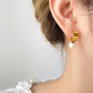 Pendientes de aro dorados en forma de C con perla blanca, mostrados en modelo para un look elegante
