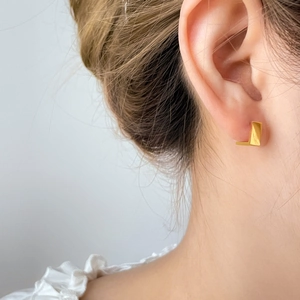 Primer plano de pendientes minimalistas en forma de L de oro de 18K con acabado pulido
