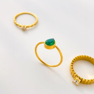 Detail shot of a minimalist gold ring with a pear-shaped green zircon and gear textures