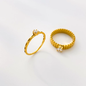 Detail of two gold plated titanium steel rings with clear zircon and ridged textures