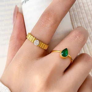 Macro shot of 18K gold textured ring with round zircon and pear-cut green emerald stone