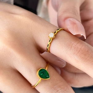 Detail of stacked gold rings featuring round clear stone and green teardrop zircon