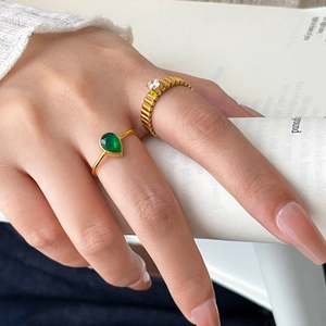 Golden stackable rings with green pear-shaped zircon and gear-textured band on a model's hand