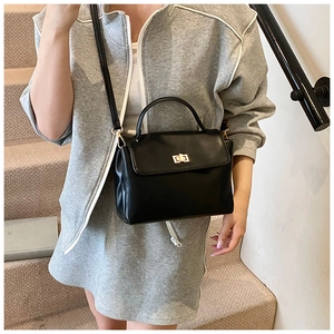 Detail of a minimalist black soft leather crossbody bag with elegant golden twist lock buckle