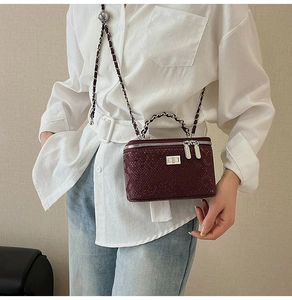 Detail of burgundy snakeskin chain bag worn with a white shirt for a luxury look
