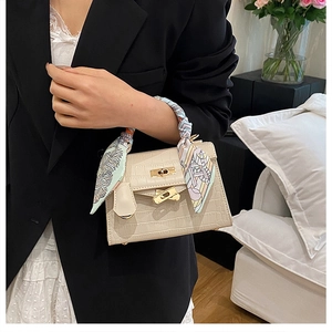 Detail of beige crocodile embossed mini handbag with silk scarf handle and gold twist lock
