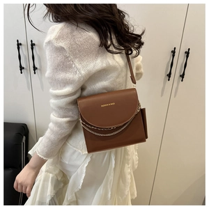 Brown leather crossbody bag with metal chain detail and adjustable strap on model
