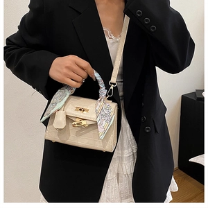 Close-up of beige crocodile pattern small handbag with silk scarf handle and gold lock