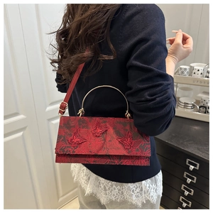 Detail view of red lace handbag with butterfly embroidery and golden metal handle