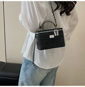Detail of a black snake-embossed box bag with silver hardware on a model's shoulder