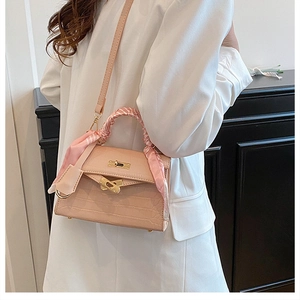 Detailed close-up of pink crocodile-textured handbag with gold lock and silk scarf wrap