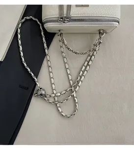 Detail of silver chain strap and smooth metal zipper on white snake pattern crossbody bag