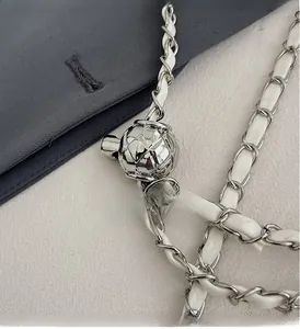Detail of silver chain strap with white leather and diamond-patterned metal adjuster ball