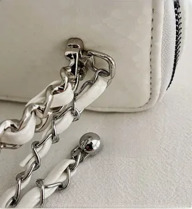 Detail of snake-embossed white bag with woven chain strap and metal ball accents