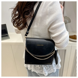 Detailed view of a black leather square crossbody bag with gold chain and metal lettering