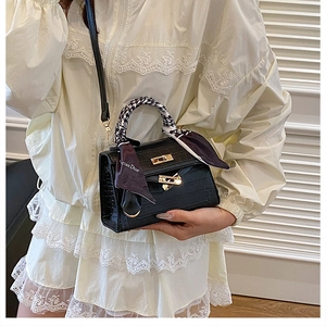 Detail view of black crocodile pattern handbag with Kelly lock and houndstooth silk scarf