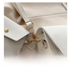 Close-up of golden metal hooks and fine chain strap on a white leather shoulder bag
