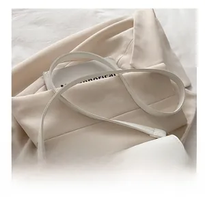 Detail of white semi-circular shoulder bag with adjustable strap on a beige blazer