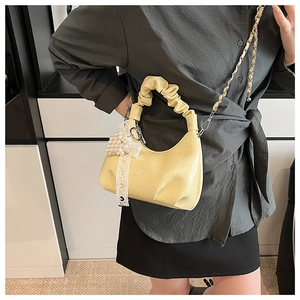 Detail of light yellow ruched bag featuring a pearl heart charm and metal chain strap