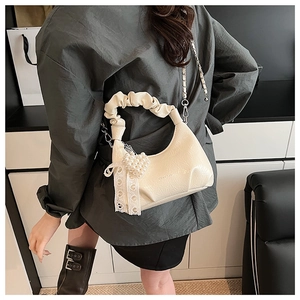 Detail of cream pleated handbag with pearl heart charm and lace bow decoration