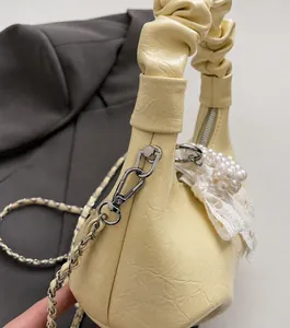 Detail of beige pleated handbag with silver chain strap and decorative pearl bow charm