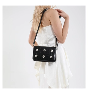 Detail of black glossy leather crossbody bag with silver rivets and sleek strap