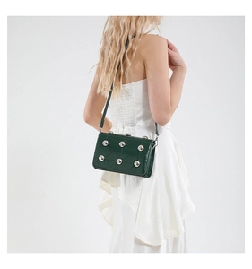 Detail of dark green punk rivet square bag worn on shoulder with shiny leather texture