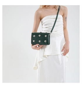 Detail of dark green studded crossbody bag with metallic beads on glossy leather