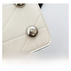Detailed macro view of white quilted leather texture with silver dome rivets on bag