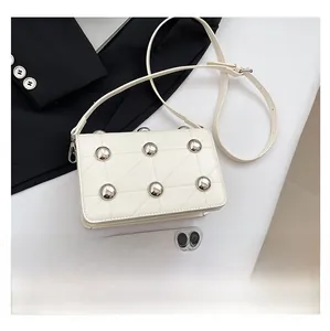 Detailed view of a white quilted crossbody bag with silver studs and adjustable strap